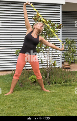 Stretching femme blonde fait son principal s'étire avec un extérieur en caoutchouc dans le jardin. Verticalement. Banque D'Images