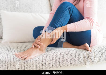 Libre woman sitting on sofa tient sa blessure à la cheville, la sensation de douleur. Concept de santé et de soins médicaux. Banque D'Images