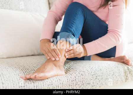 Libre woman sitting on sofa tient sa blessure à la cheville, la sensation de douleur. Concept de santé et de soins médicaux. Banque D'Images