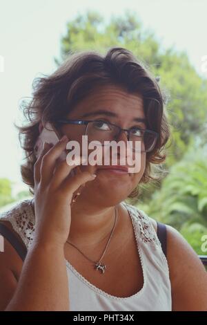 Femme millénaire, avec un téléphone mobile dans la main, l'écoute, avec les yeux et d'un ennuie / expression douteuse Banque D'Images