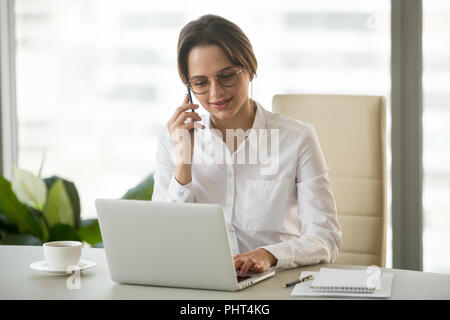 Millénaire réussie businesswoman using laptop talking on phone Banque D'Images