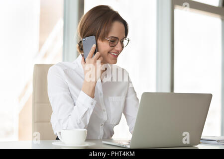 Smiling confident businesswoman making phone call using laptop i Banque D'Images