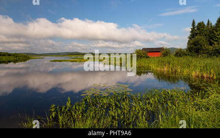 Un paysage tranquille vue d'un petit abri de pêche rouge sur la rivière Eel, Benton, Nouveau Brunswick, Canada. Les nuages blancs moelleux reflète dans l'eau. Banque D'Images
