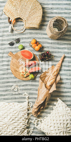 Pique-nique d'été. Vin rose en verre et la bouteille, fruits frais à bord, de la baguette sur la couverture et la femme Sac de paille, vue du dessus. Rassemblement en plein air ou Banque D'Images