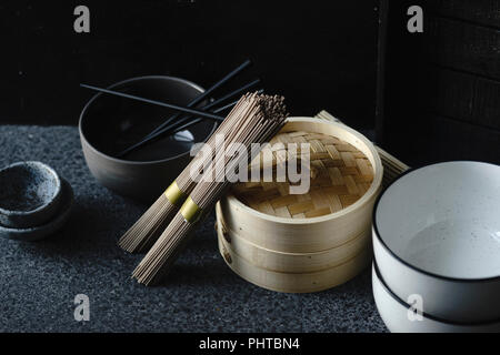 Nouilles Soba, bateau à vapeur de bambou et une cuisine asiatique props sur fond sombre Banque D'Images