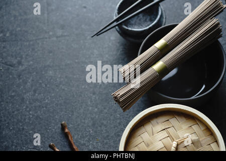 Nouilles Soba, bateau à vapeur de bambou et une cuisine asiatique props sur fond sombre with copy space Banque D'Images