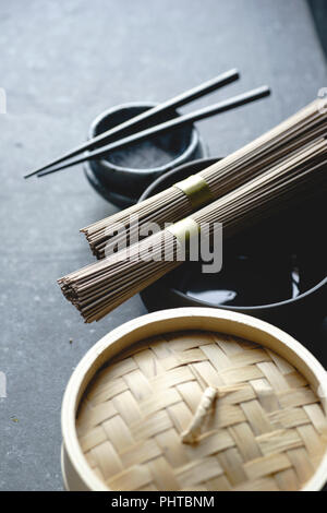 Nouilles Soba, bateau à vapeur de bambou et une cuisine asiatique props sur fond sombre Banque D'Images