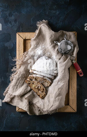 Tranches de gâteau de Noël traditionnel allemand, cuisson festive. Les stollen avec raisins secs et le sucre en poudre sur le linge de maison serviette, plateau en bois, tamis vintage Banque D'Images