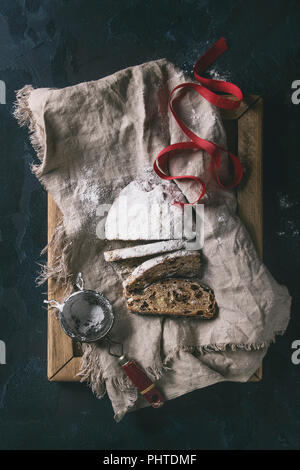 Tranches de gâteau de Noël traditionnel allemand, cuisson festive. Les stollen avec raisins secs et le sucre en poudre sur le linge de maison serviette, plateau en bois, tamis, ri rouge Banque D'Images