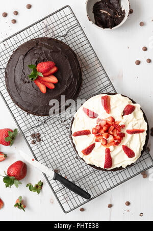 Préparation de gâteau au chocolat ; une moitié avec glaçage au chocolat et l'autre couvert de crème et couper les fraises. Banque D'Images