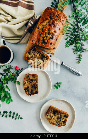 Pain aux courgettes au chocolat avec des noix en tranches sur une planche à découper en bois et servis sur deux plaques blanches accompagné d'une tasse de thé, vert laisse un Banque D'Images