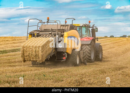 Un tracteur Massey Ferguson 7618 et New Holland 1290 Bigbaler travaillant sur la paille d'orge avec un fini de décharger la balle Banque D'Images