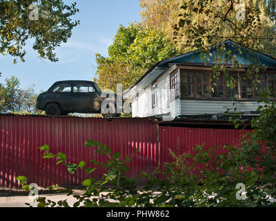 Près d'un bâtiment blanc avec de grandes fenêtres derrière une clôture rouge sur le toit d'un hangar est une vieille voiture rétro à l'automne lors d'une journée ensoleillée à proximité d'arbres avec y Banque D'Images