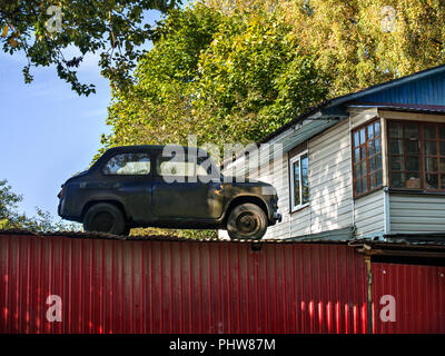 Une vieille voiture rétro se tient sur le toit d'une grange derrière une clôture rouge près d'une maison blanche avec de grandes fenêtres sur un beau jour d'automne clair, Close up Banque D'Images