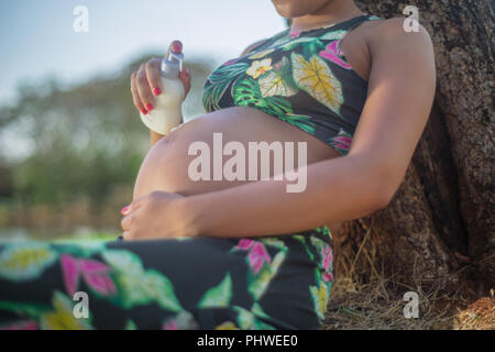 Femme enceinte dans un parc en mettant de la crème sur son ventre pour éviter les vergetures. Banque D'Images