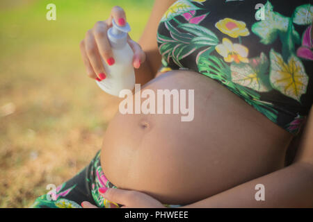 Femme enceinte dans un parc en mettant de la crème sur son ventre pour éviter les vergetures. Banque D'Images