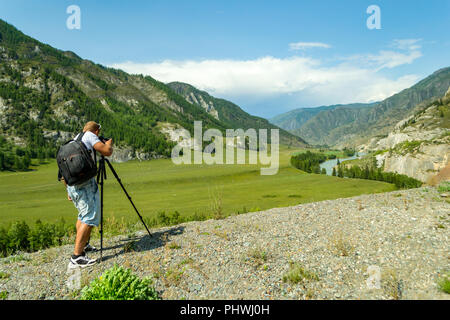 Un homme photographe est la mise en place d'un comité permanent de l'appareil photo sur un trépied au-dessus d'un rocher dans les montagnes de l'Altaï fait une photo d'une rivière d'une turquoise Banque D'Images