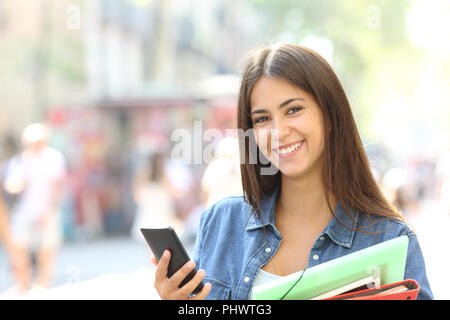 Happy student posing looking at camera détenant un téléphone intelligent et des dossiers dans la rue Banque D'Images