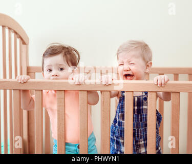 Portrait de deux adorables bébés mignon drôle frères et sœurs les amis de neuf mois au lit permanent lit-bébé suçant manger mâcher côtés en bois de pleurer, à la recherche dans Banque D'Images