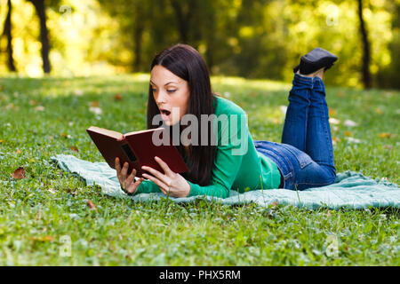 Surpris woman reading book in park Banque D'Images