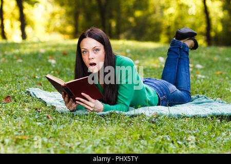 Surpris woman reading book in park Banque D'Images