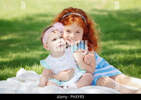 Portrait of two cute adorable petite rousse Caucasian girls soeurs frères et sœurs des enfants, assis ensemble dans le champ prairie parc à l'extérieur, serrant, loo Banque D'Images