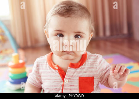 Closeup portrait of cute adorable blonde Woman smiling enfant garçon aux yeux bleus assis sur le plancher dans les enfants à manger. Petit bébé jouant avec de Banque D'Images