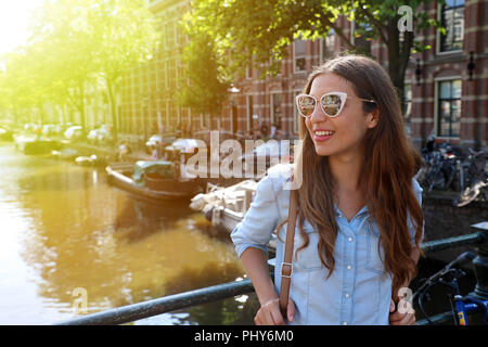 Portrait de belle fille joyeuse avec des lunettes à la recherche sur le côté sur l'un des canaux typiques d'Amsterdam, Pays-Bas. La lumière filtre vintage flare. Banque D'Images