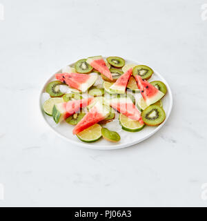 Les fruits frais. Dans un bol, des morceaux de citron vert, pastèque, kiwi et des cubes de glace sur une table en marbre gris avec une copie de l'espace. Dessert Banque D'Images