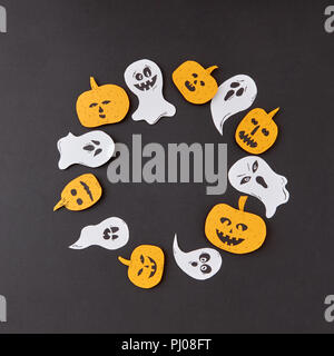 Cadre décoratif de round battant la main flottant esprit fantômes et citrouilles jaune souriant sur un fond de papier noir. Banque D'Images