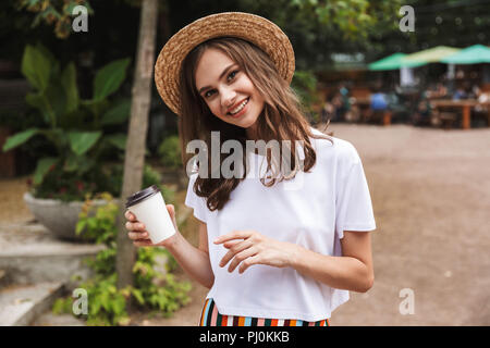 Happy young girl holding Coffee cup à emporter tout en se tenant à l'extérieur du parc Banque D'Images