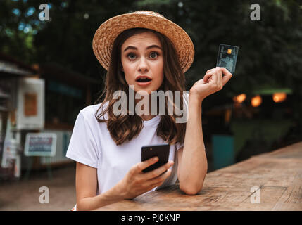 Young Girl holding a choqué de carte de crédit en plastique lors de l'utilisation du téléphone mobile au café en plein air Banque D'Images