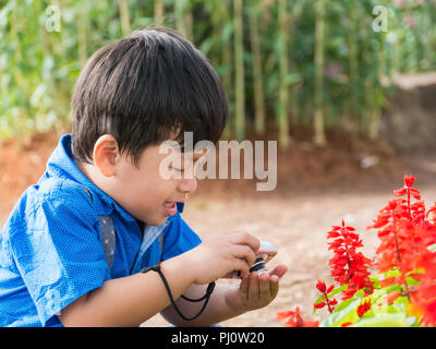 Petit garçon asiatique prendre caméra sur fleur de jardin, Banque D'Images