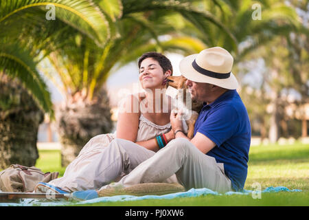 Cheerful couple bénéficiant d'une activité de loisirs assis sur l'herbe verte en ville et jouer avec les jeunes chiens fous baisers shetland beaucoup. l Banque D'Images