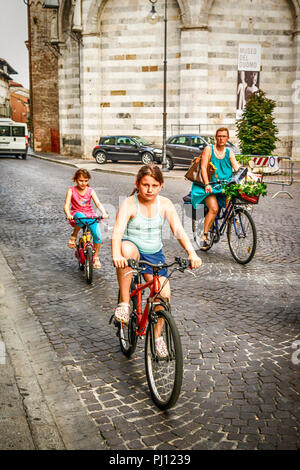 Mère de famille et ses deux enfants à vélo dans les rues d'Udine, Italie Banque D'Images