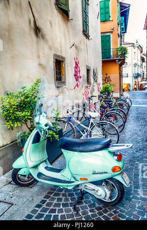 Un aqua bleu Vespa scooter garé à côté d'une rangée de vélos dans une rue d'Udine, Italie Banque D'Images