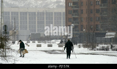 5 mars 1993 pendant le siège de Sarajevo : à l'arrière de l'hôtel Holiday Inn, un homme avec une béquille promenades dans la neige. Un autre jeune homme porte plusieurs conteneurs en plastique vides, sur sa façon de collecter de l'eau. C'est territoire de sniper, mais fine neige qui offre un degré de couverture. Banque D'Images