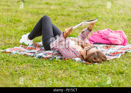 Belle jeune femme chemise à carreaux en verres de port fixe et reposant sur l'herbe verte, elle livre de lecture en été ou au printemps, vue du dessus Banque D'Images