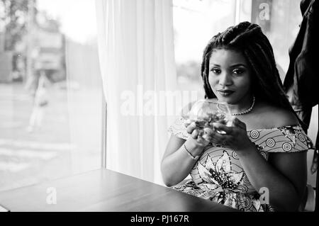 Hauteur petit mignon african american girl avec des dreadlocks, d'usure au niveau de la couleur jaune robe, assis au café avec fleur à verre. Noir et blanc. Banque D'Images