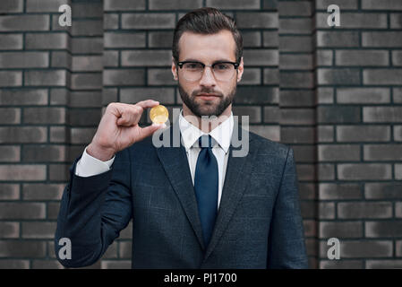 Photo de beau riche homme d'affaires en litige montrant l'accent sur bitcoin or camera Banque D'Images