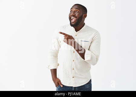 Homme d'être surrpsied avec incroyable d'artifice en son honneur, la célébration de b-jour avec des amis. Beau joyeux african american guy avec barbe en chemise blanche pointant et contemplant joyeusement à l'angle supérieur gauche Banque D'Images