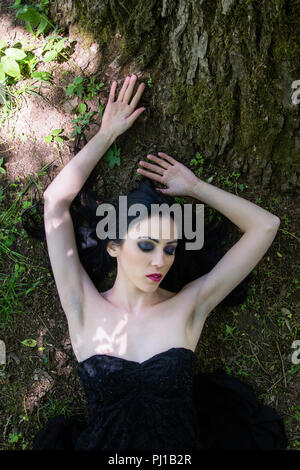 Femme en robe noire pâle allongé sur le sol en bois, scène mystère sombre Banque D'Images
