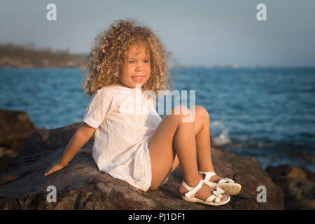 Petite fille en robe blanche sur un rocher près d'une mer Banque D'Images