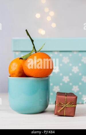 Mandarines biologiques dans une tasse en céramique bleu, et petit cadeau sur fond blanc avec bokeh Banque D'Images