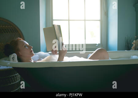 Woman Reading book dans une baignoire à bains Banque D'Images