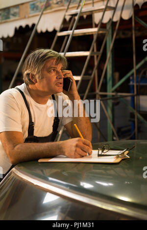 Mécanicien mâle talking on mobile phone while writing on clipboard Banque D'Images