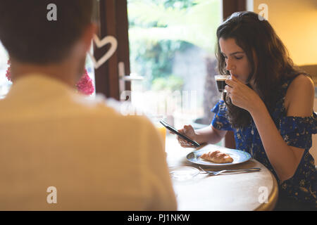 Woman using mobile phone while having coffee Banque D'Images