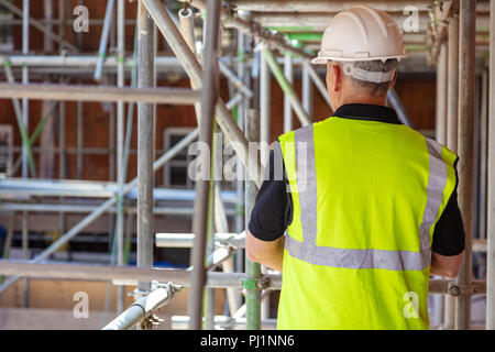 Vue arrière de l'homme constructeur construction worker on construction site wearing hard hat et Gilet haute visibilité Banque D'Images