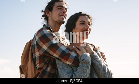 Jeune homme avec sac à dos se tenant sur sa femme à l'écart et souriant. Loving couple looking at a voir et avec le sourire sur le visage. Banque D'Images