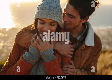 Close up portrait of young couple on winter holiday. Beau jeune homme embrassant sa petite amie par derrière dans une journée d'hiver. Banque D'Images